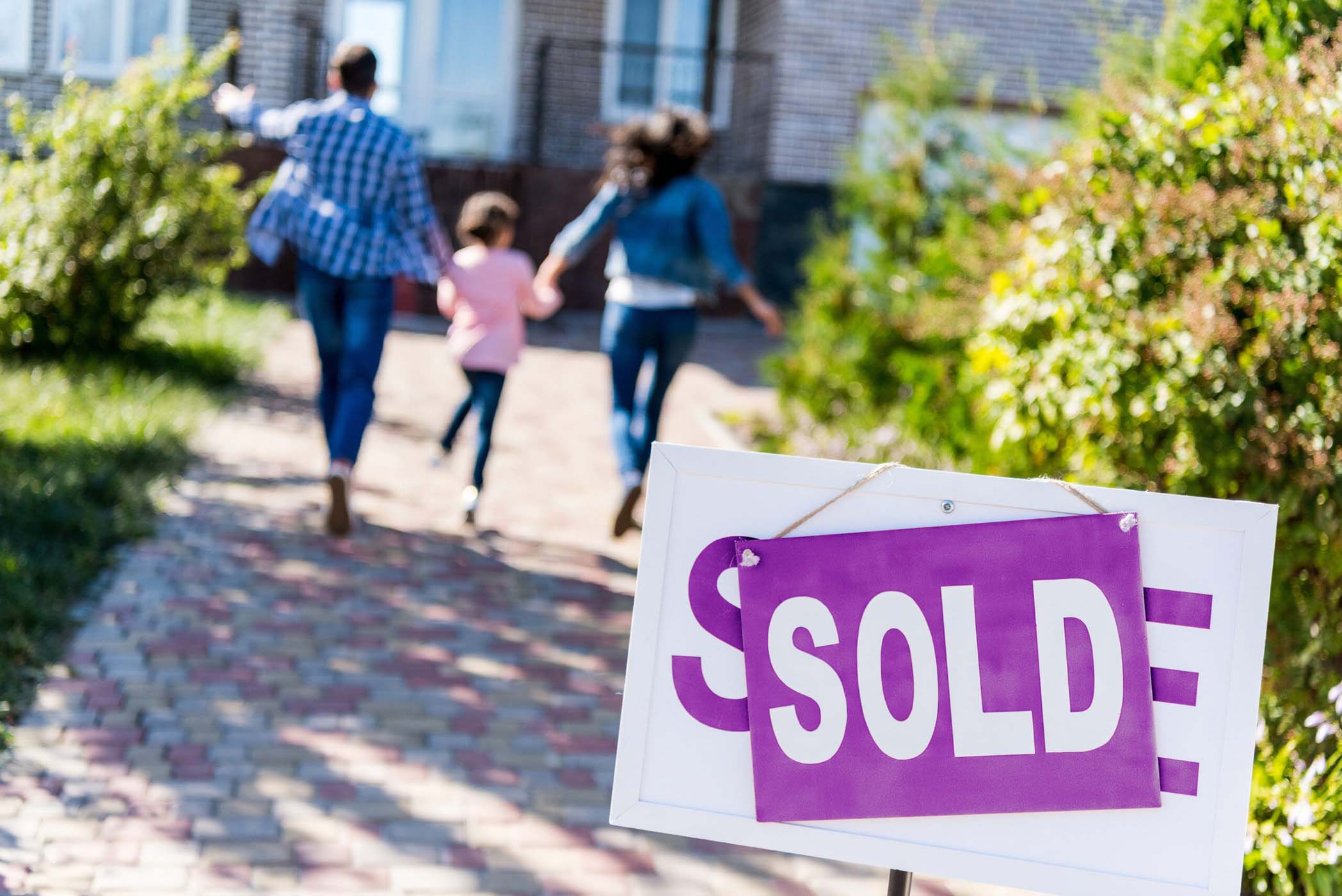 A family walking into their new home, with a sign that says sold
