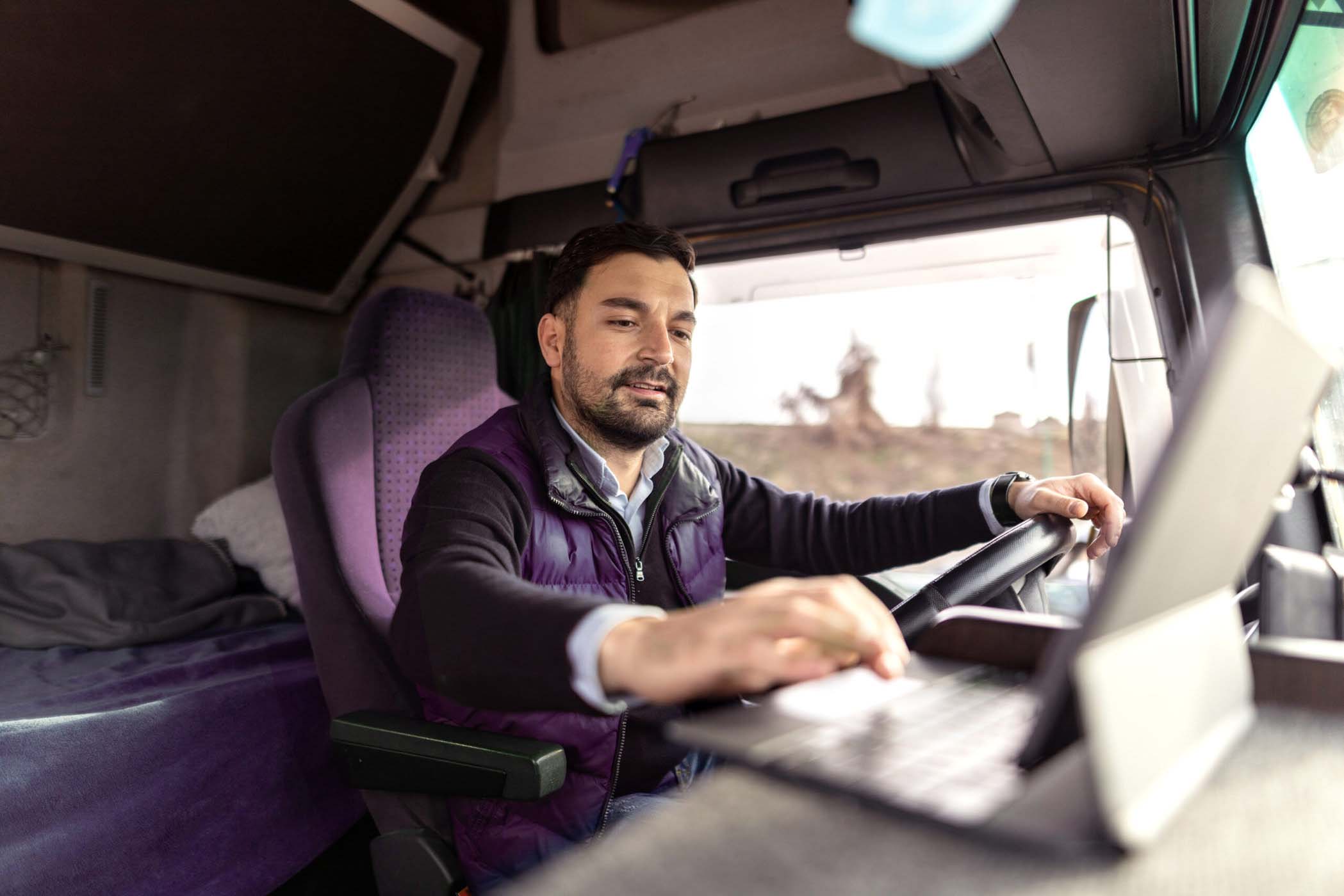 Young truck driver typing destination on tablet while sitting in truck cabin