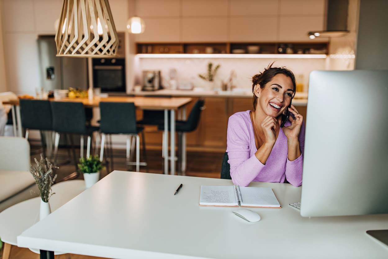 A girl laughing on the phone, sitting in front of a computer