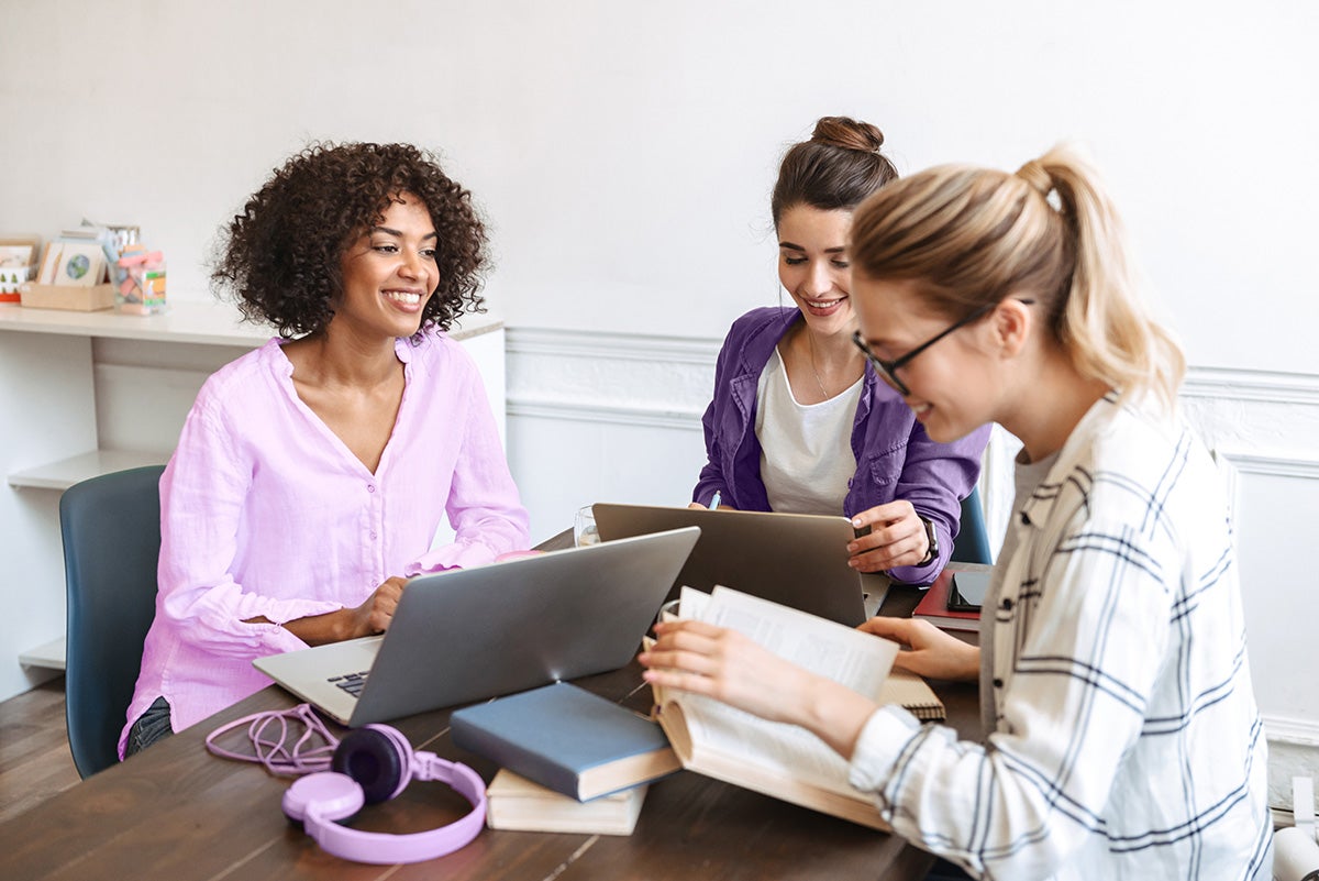 3 women on laptops with books