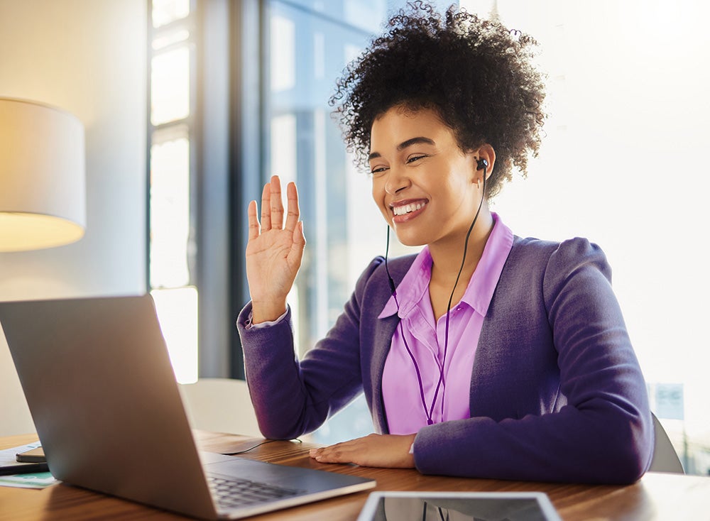 Woman smiling at laptop and holding her hand up