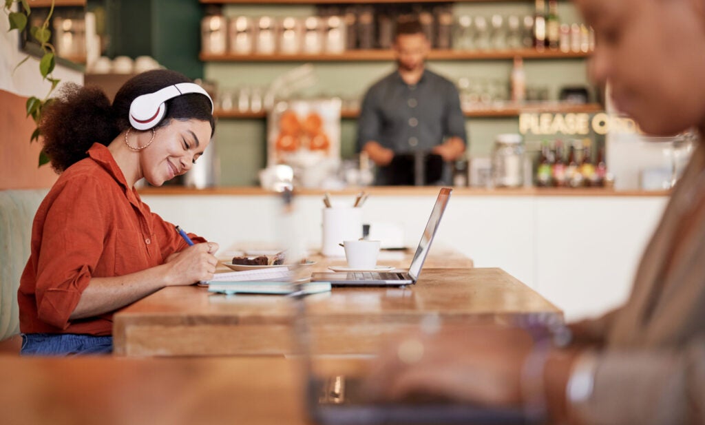 woman working on a laptop in a cafe with a man at the counter in the background
