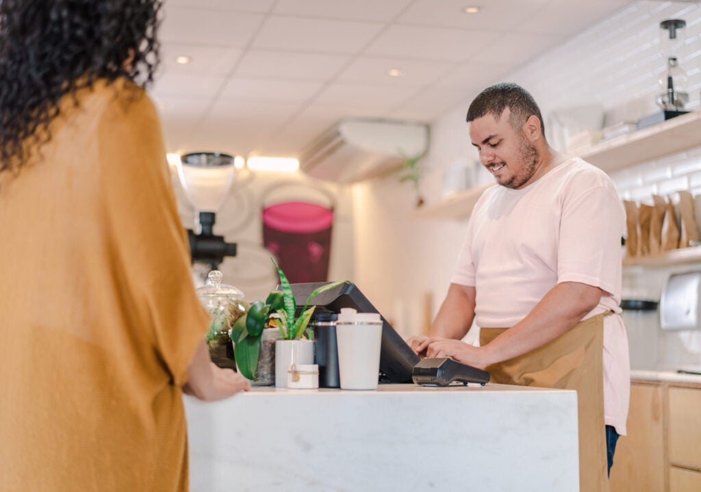 Man using a screen device at a desk with a woman waiting